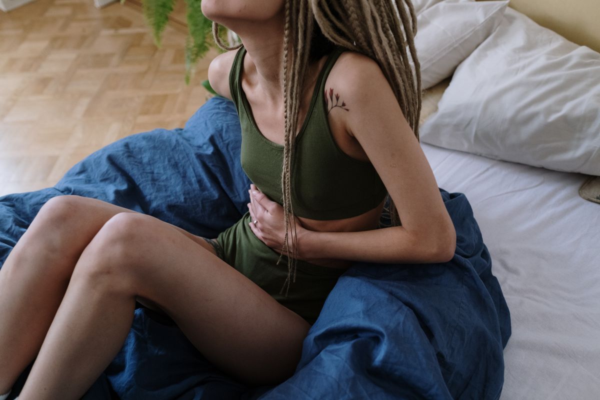 A woman sitting on a bed with abdominal discomfort